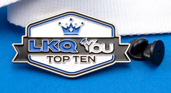 Hexagonal enamel lapel pin with crown icon and text reading LKQ You Top Ten, displayed with a white ribbon and black rubber clutch backs on a blue background.