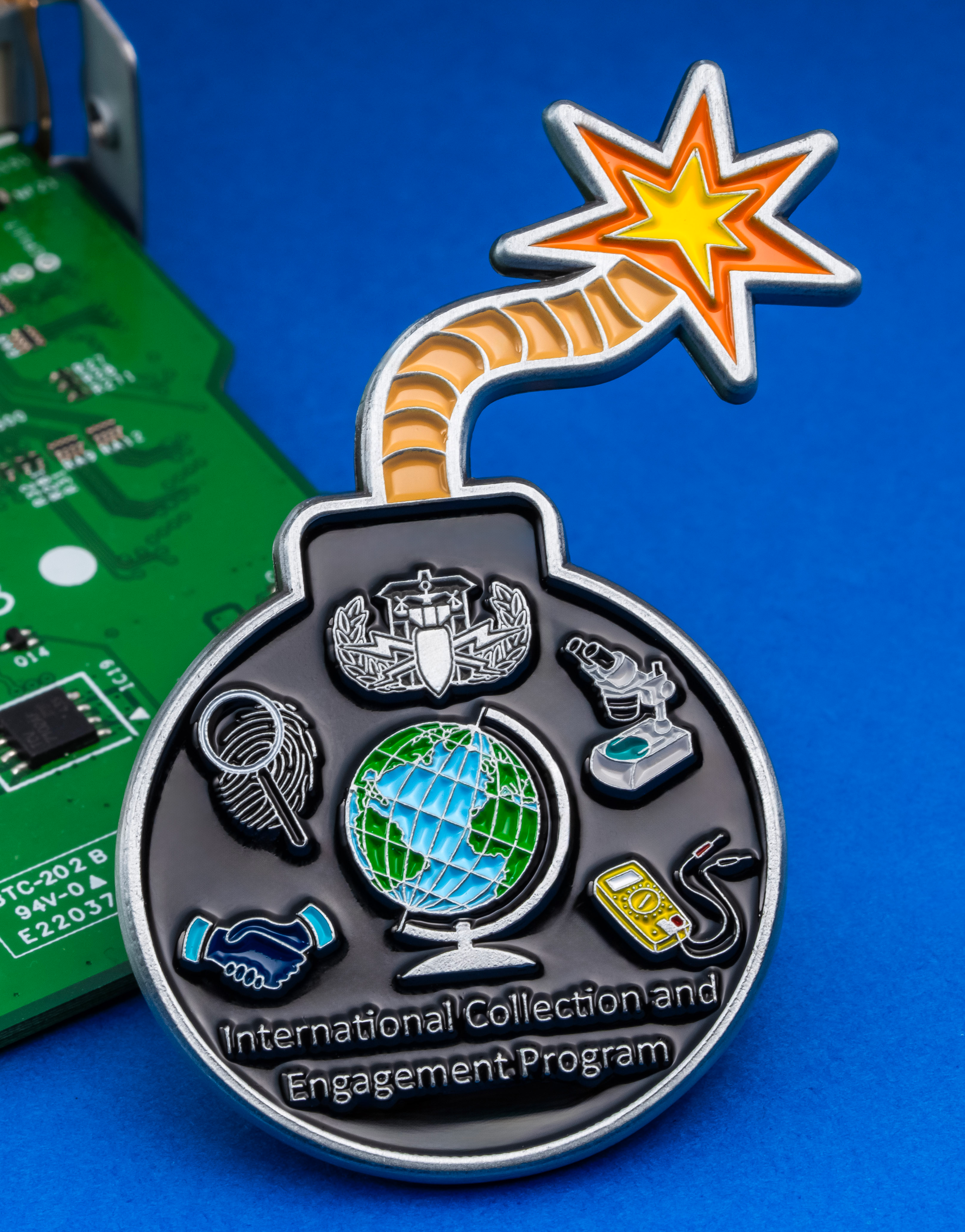 Enamel bomb-shaped lapel pin with a lit fuse, featuring global and scientific icons for the International Collection and Engagement Program.