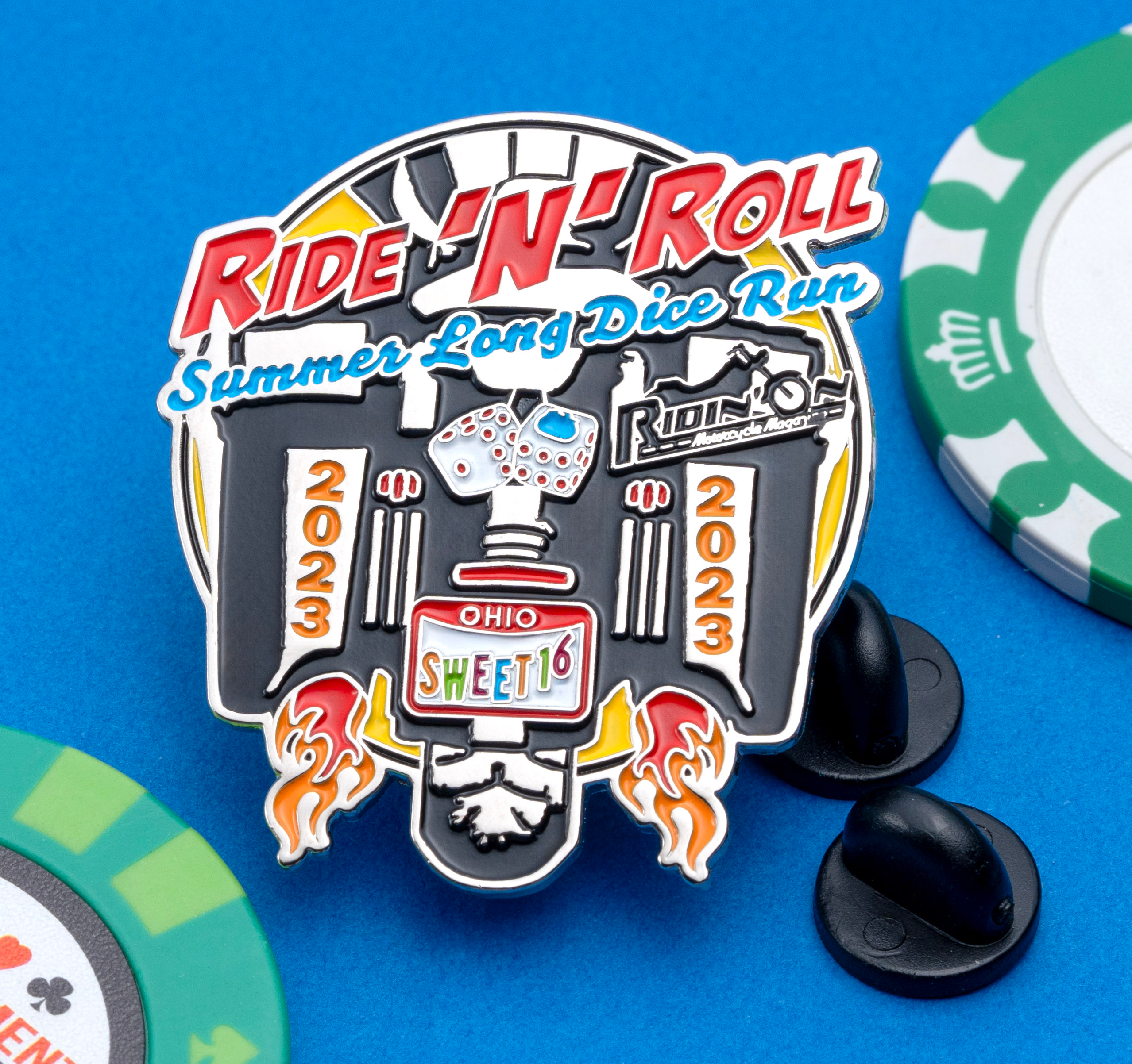 Soft enamel lapel pin for Ride 'N' Roll Summer Long Dice Run 2023, featuring motorcycle graphics and dice, surrounded by poker chips on a blue background.