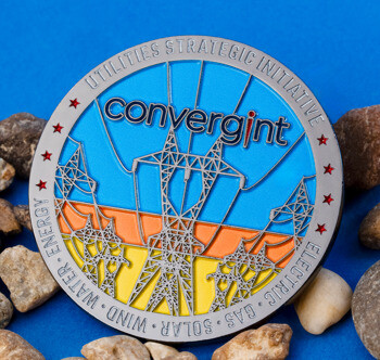 Convergint Utilities Strategic Initiative challenge coin featuring power line towers over a blue, orange, and yellow background, resting on small stones.