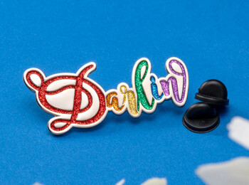 Darlin script lapel pin featuring rainbow glitter fill on a silver base with black rubber backings.