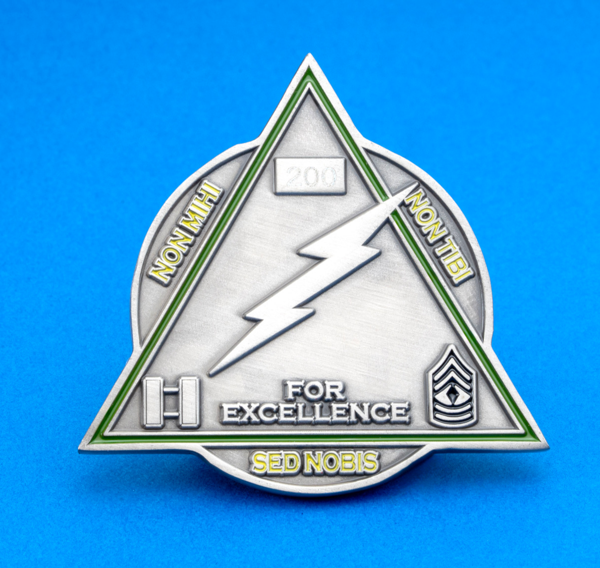 Triangular challenge coin with a lightning bolt, military rank insignias, and the text For Excellence.