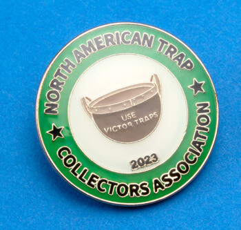 Round lapel pin for the North American Trap Collectors Association featuring a Victor Trap illustration and green border.