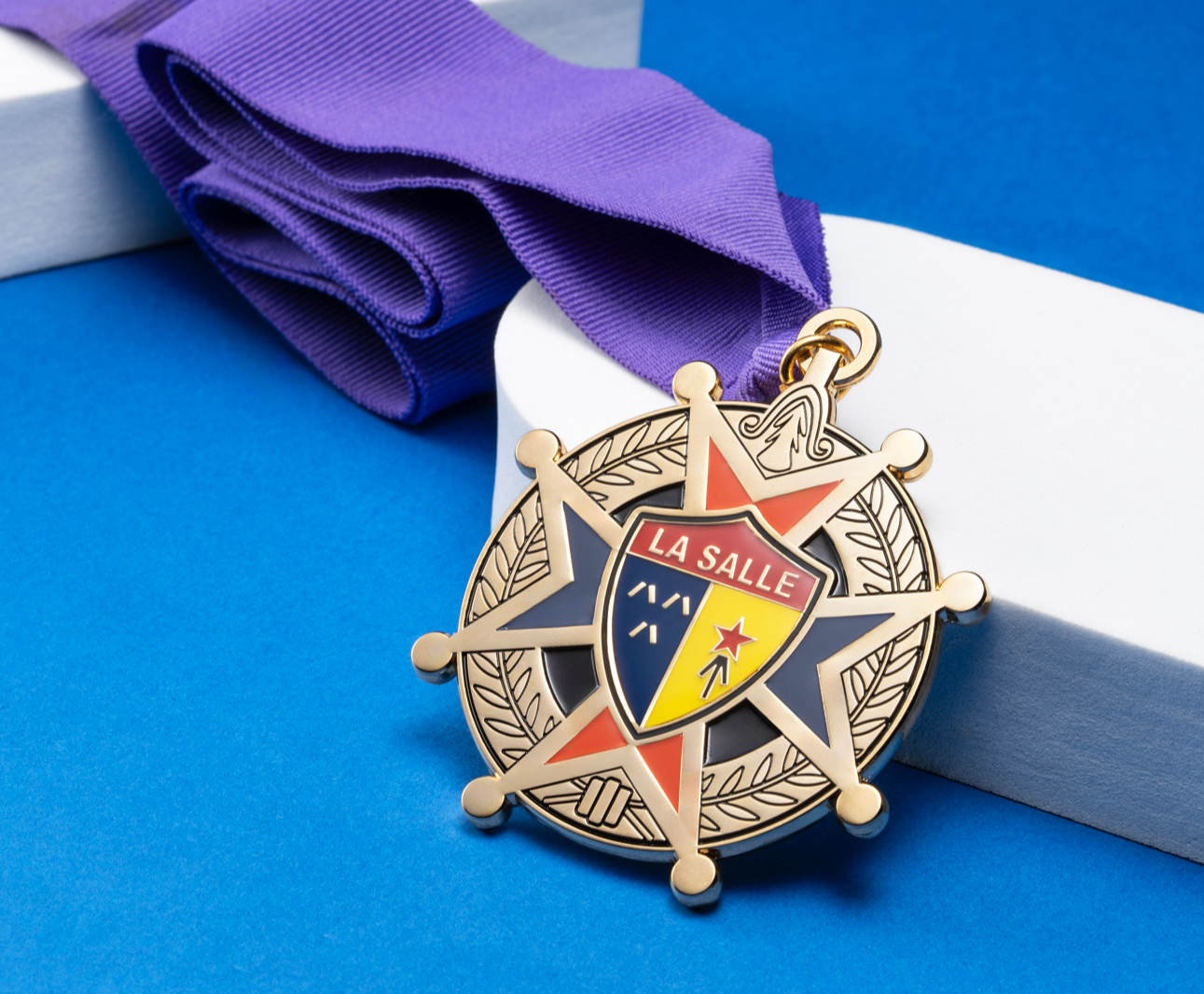 Gold medal with a purple ribbon featuring the La Salle crest on a star-shaped design with blue, orange, and yellow enamel.