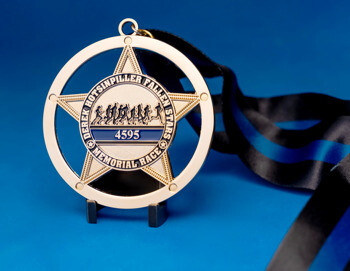 Gold star-shaped medal with a circular cutout featuring runners and a blue line ribbon for the Derek Hotsinpiller Fallen Stars Memorial Race.