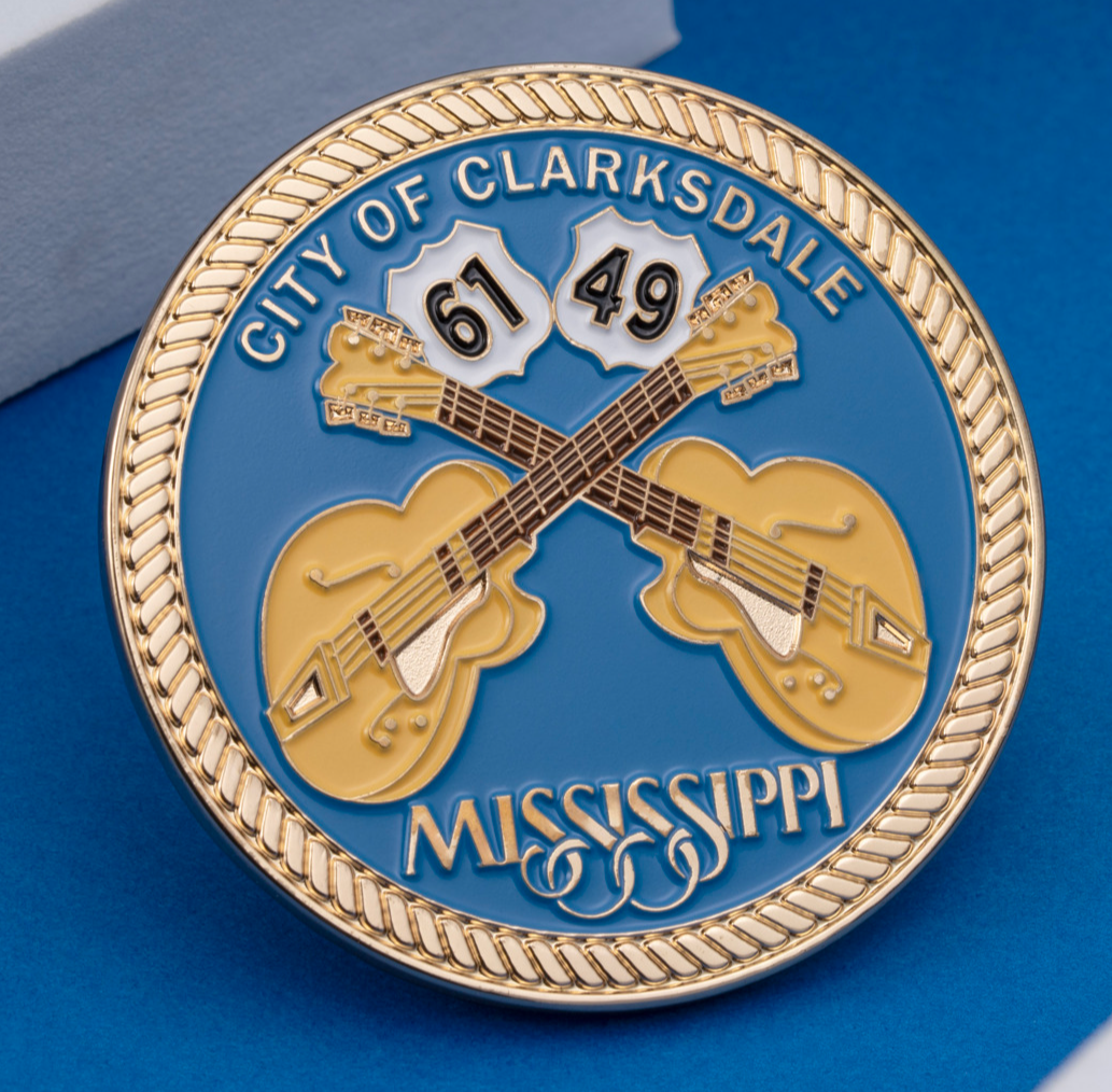 Circular blue challenge coin featuring crossed yellow guitars, highway signs 61 and 49, and a gold rope border for the City of Clarksdale, Mississippi.