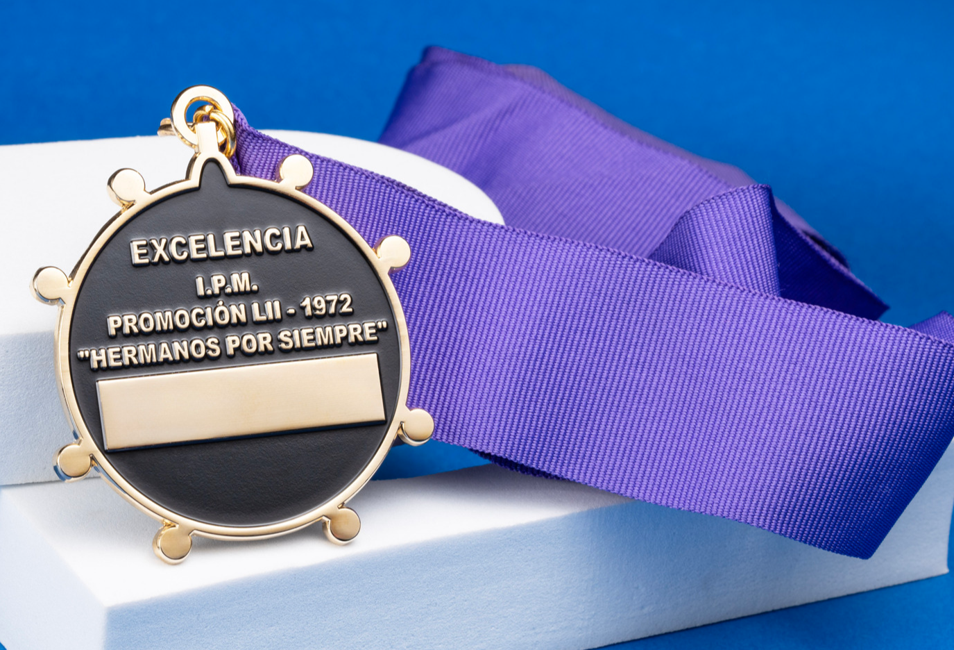 Gold and black circular medal with a purple neck ribbon featuring the text Excelencia I.P.M. Promoción LII - 1972.