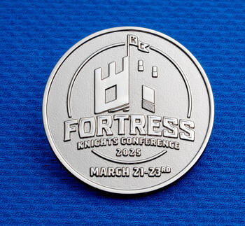 Silver Fortress Knights Conference 2025 challenge coin with a castle icon on a blue textured background.