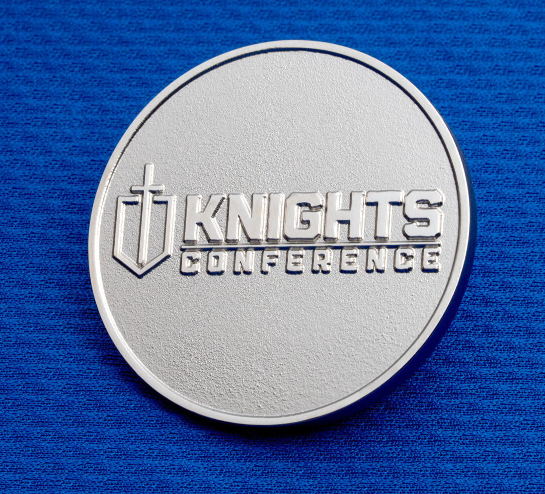Silver Knights Conference challenge coin featuring a sword and shield emblem on a blue textured background.