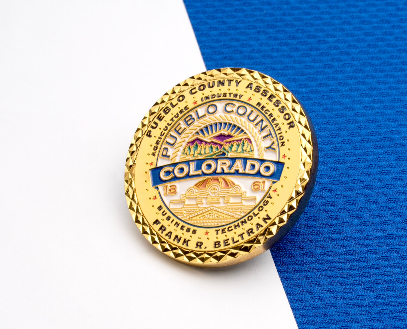 Gold challenge coin for Pueblo County Assessor Frank R. Beltran featuring a Colorado mountain scene and diamond-cut edge.