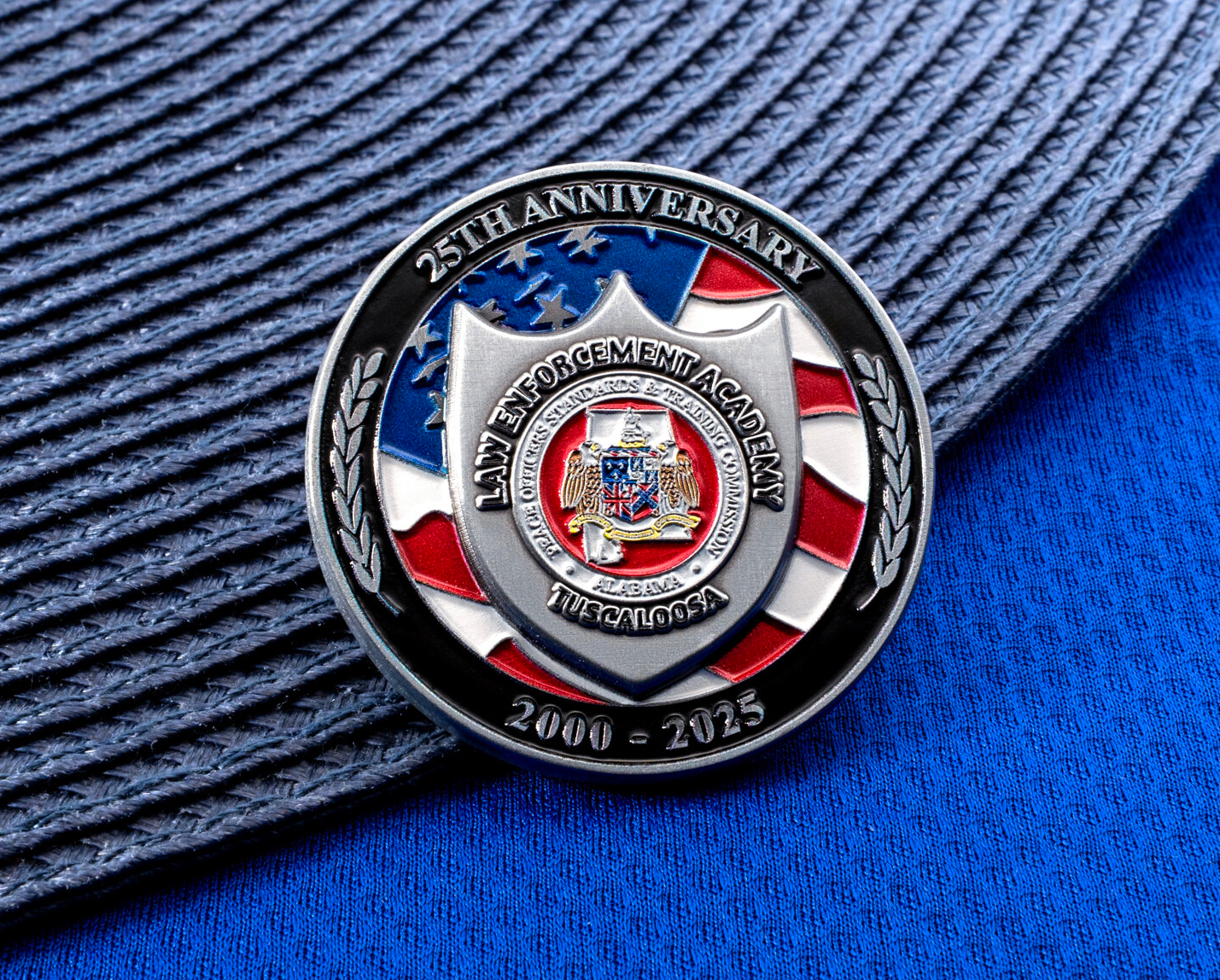Law Enforcement Academy Tuscaloosa 25th Anniversary challenge coin with American flag background and silver shield emblem.