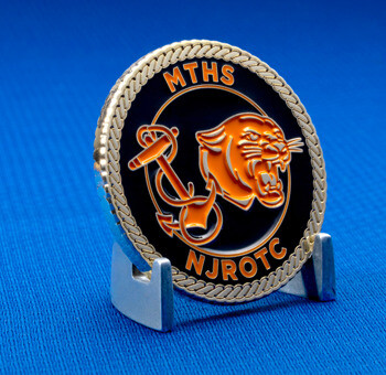 Round challenge coin featuring MTHS NJROTC text with an orange panther head and anchor design on a black background with a rope border.