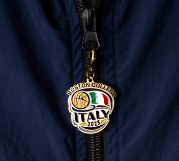 Boston College Italy 2023 basketball enamel zipper pull with Italian flag colors on a blue jacket zipper.