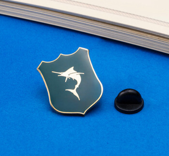 Shield-shaped lapel pin with a green enamel background and a white marlin silhouette, shown with a black rubber clutch.