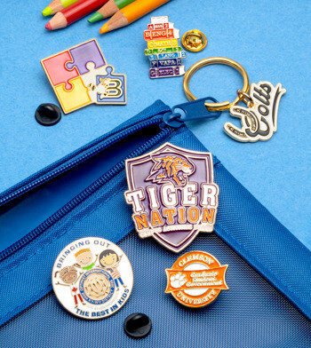Assorted school-themed lapel pins and a Colts keychain arranged on a blue pencil case with colored pencils.