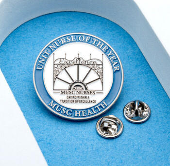 Round lapel pin featuring a blue border with 'Unit Nurse of the Year' and 'MUSC Health' text surrounding a gate design.