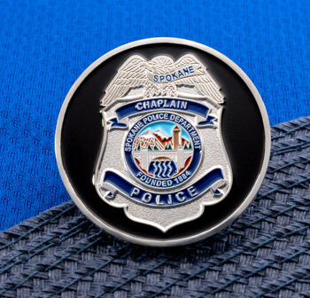 A silver challenge coin featuring the Spokane Police Department chaplain badge emblem on a black background.