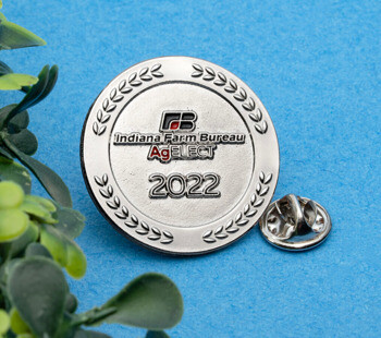Round silver lapel pin for Indiana Farm Bureau AgELECT 2022 with a laurel wreath border on a blue background.