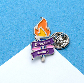 Enamel lapel pin featuring an orange and yellow torch with a purple banner reading Directors Award.