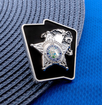 Silver lapel pin featuring the Lee County Sheriff's Office star and seal on a black state map background.