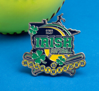 Custom softball lapel pin featuring green 'Irish' text, 12U designation, shamrocks, and player numbers against a blue background next to a softball.