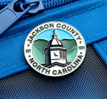 Enamel lapel pin for Jackson County North Carolina featuring a clock tower and mountain landscape on a blue zipper pouch.
