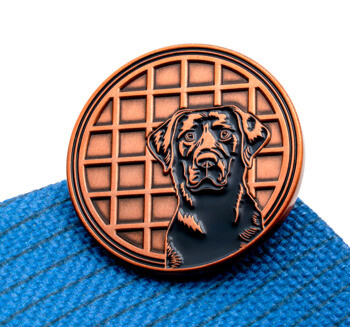 Circular lapel pin featuring a black labrador retriever head over an antique copper grid pattern.