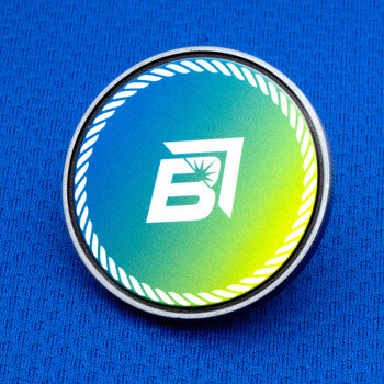 Circular challenge coin featuring a stylized white B emblem with a sunburst on a blue, green, and yellow gradient background with a rope border design.