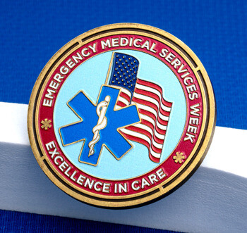 Emergency Medical Services Week challenge coin featuring a Star of Life, American flag, and Excellence in Care text over a blue and red enamel background.