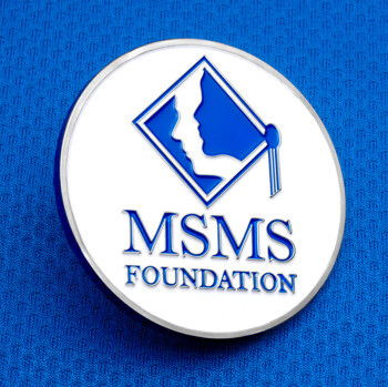 MSMS Foundation custom challenge coin featuring a blue and white emblem with two faces in silhouette and a graduation tassel, set against a blue fabric backgrou