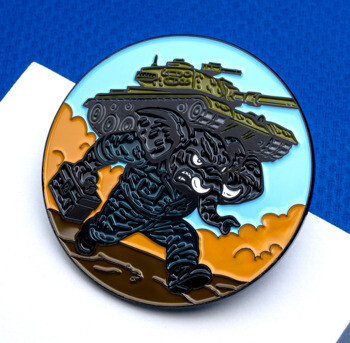 Circular lapel pin featuring a stylized black cartoon elephant carrying a military tank on its back.