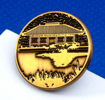 Round gold challenge coin featuring an engraved traditional East Asian pavilion with a pond and trees.