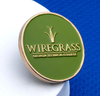 Circular green enamel lapel pin with gold trim, featuring the Wiregrass Georgia Technical College logo on a textured blue background.