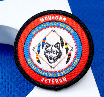Circular embroidered Mohegan Veteran patch with a wolf emblem and crossed arrows on a blue and white background.