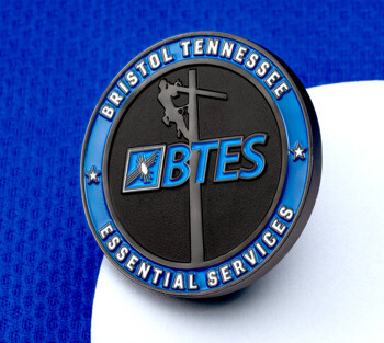 Bristol Tennessee Essential Services (BTES) circular lapel pin featuring a utility worker climbing a pole against a black and blue background.