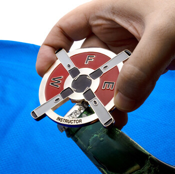 A hand using a circular red and white bottle opener challenge coin with crossed oars and FEW Instructor text to open a green glass bottle.