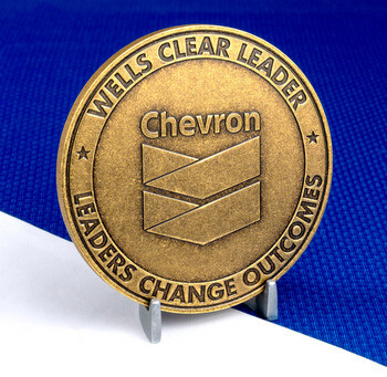 Chevron Wells Clear Leader brass challenge coin on a stand against a blue and white background