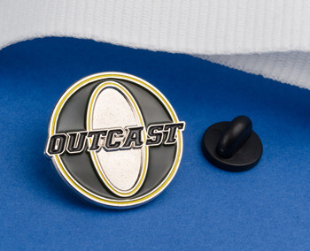 Circular black and silver lapel pin featuring the word Outcast over a silver oval with yellow accents and a black rubber clutch.